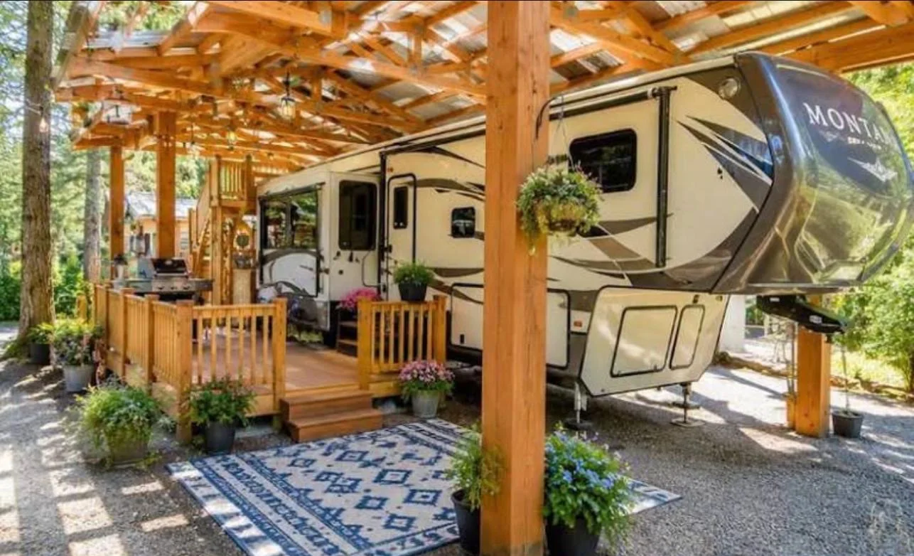 Reference photo of a fifth-wheel beside a cedar pergola with a wood deck, flower pots and an outdoor rug