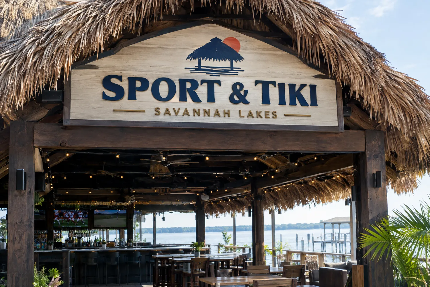 Concept view of the Sport and Tiki entrance with a carved sign under a thatched roof and the lake beyond the bar